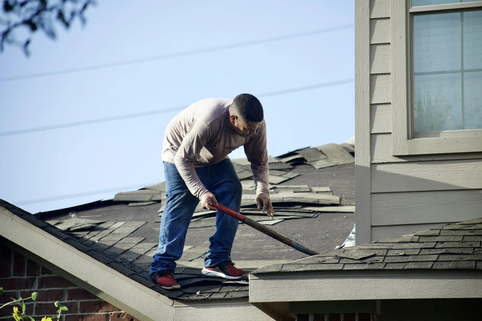 A worker tearing off old shingles on a house roof